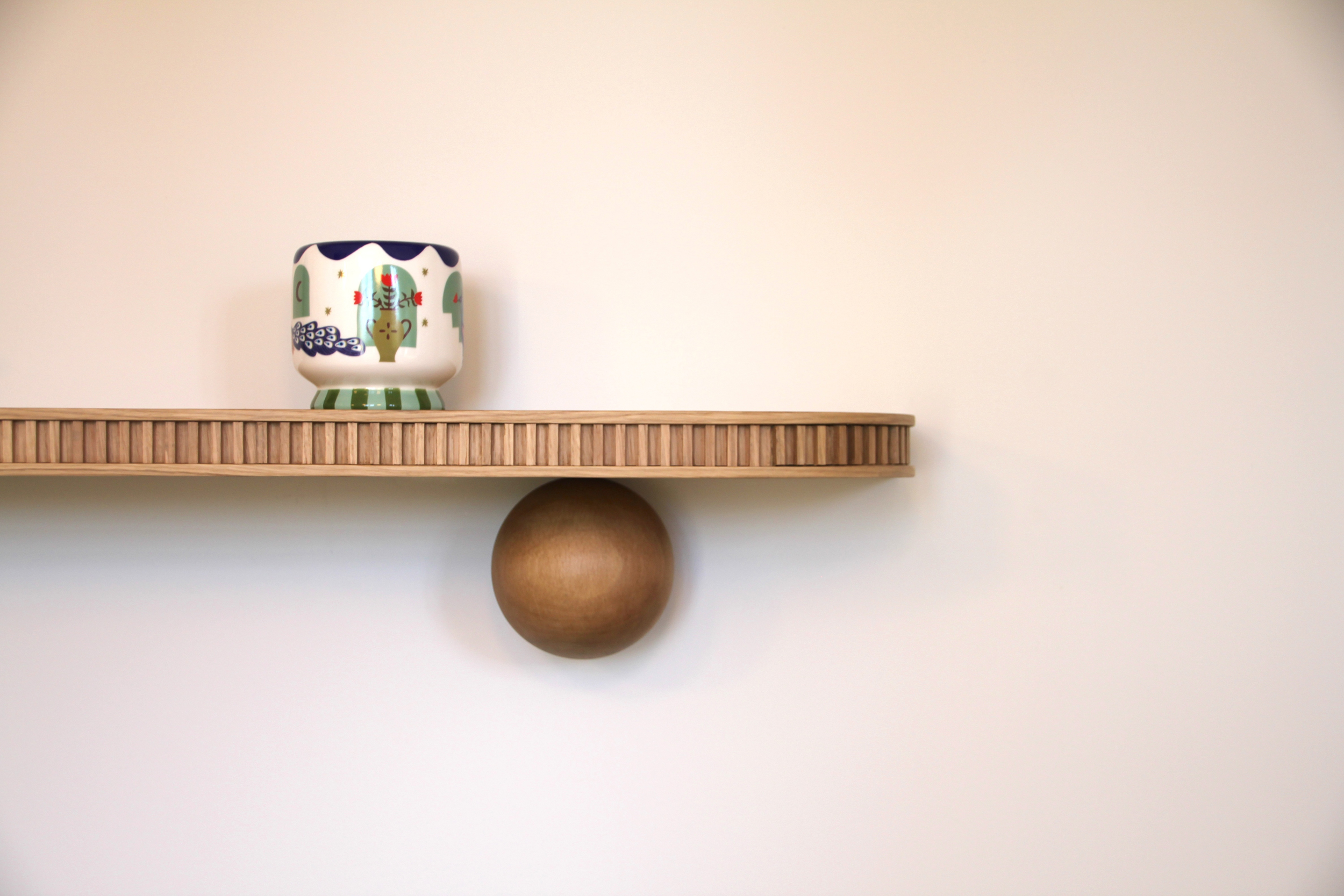 Détail d’une étagère en bois sur console boule avec un vase en céramique