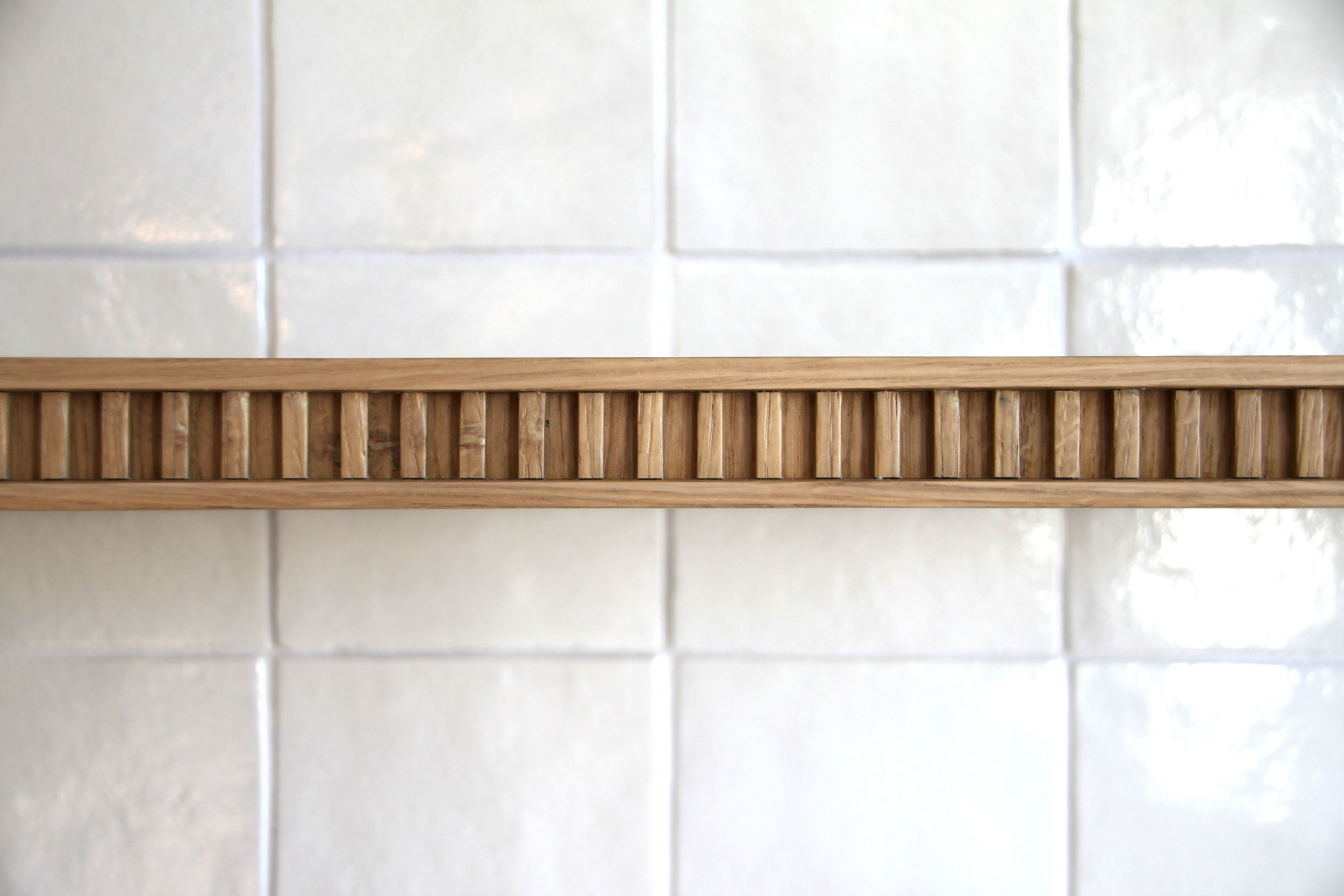 Détail d’une moulure en bois cannelé sur carrelage blanc
